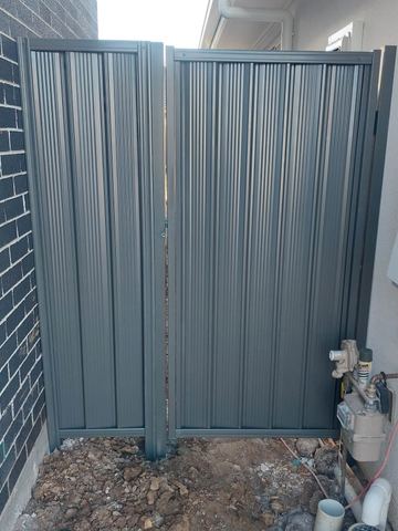 Close view of a mid grey Colorbond pedestrian gate beside conduit and a meter box