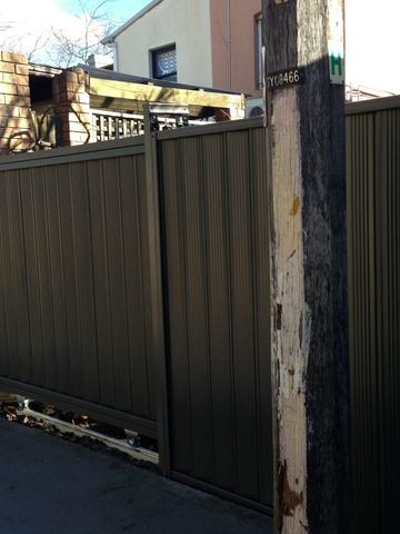 Dark Colorbond sliding driveway gate closing across a garage apron