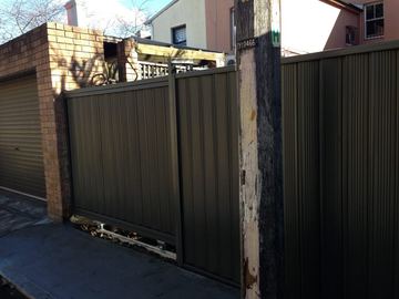 Dark Colorbond sliding driveway gate closing across a garage apron