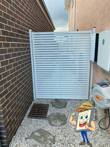 White slat gate on gravel and stepping stones closes a side passage between dark and light brick walls.