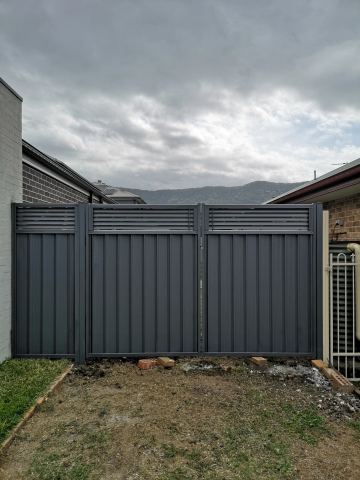Charcoal panels with louvre tops include a double swing gate set between brick houses on rough ground.