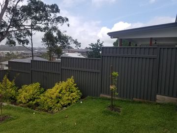 Stacked charcoal panels on pale sleepers terrace down a garden bed of bright yellow shrubs under cloudy skies.