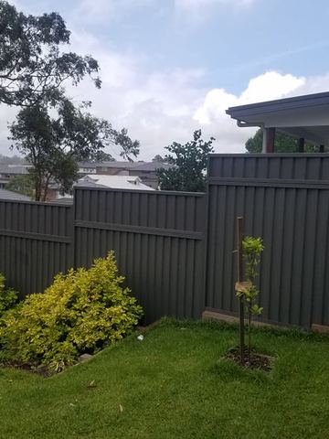Stacked charcoal panels on pale sleepers terrace down a garden bed of bright yellow shrubs under cloudy skies.