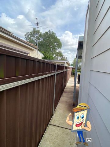 Brown Colorbond privacy fence running along a side passage beside weatherboard cladding