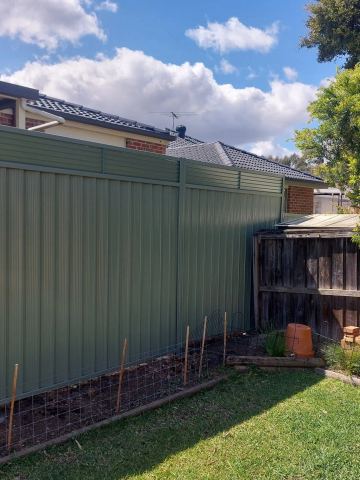 Green Colorbond privacy fence with a slat topper along a backyard boundary