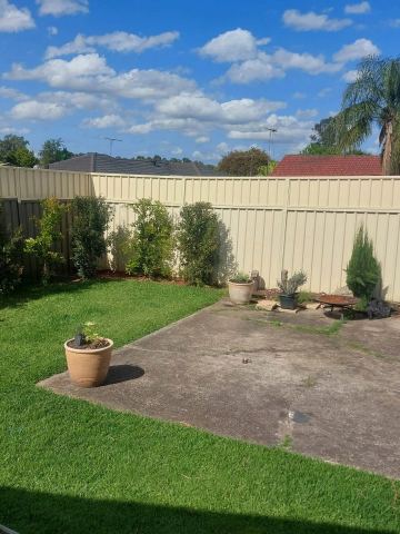 Cream panels enclose a lawn corner with shrubs, a fire pit on pavers and neighbouring roofs beyond.