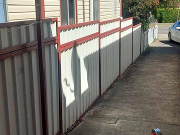 Cream corrugated sheets in heritage-red frames step along a concrete side drive beside weatherboard cladding.