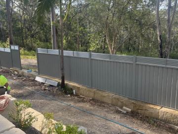 Mid grey Colorbond privacy fence running along a bushland boundary on a dirt yard