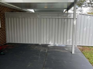 White Colorbond fence with a slat topper under a carport on a dark concrete slab