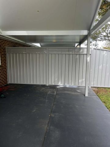 White Colorbond fence with a slat topper under a carport on a dark concrete slab