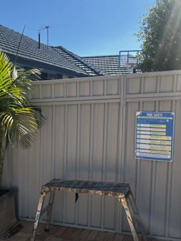 Cream Colorbond privacy fence with a potted palm and a step stool on a paved courtyard