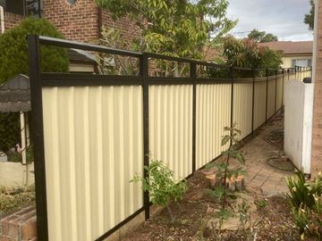 Cream Colorbond privacy fence with black posts and rails along a garden boundary