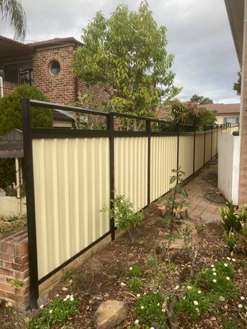 Cream Colorbond privacy fence with black posts and rails along a garden boundary