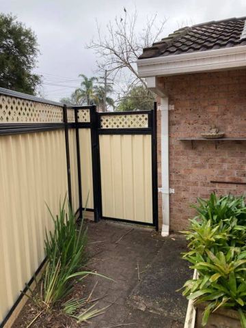 Cream Colorbond pedestrian gate with a lattice top in a black frame beside a brick wall