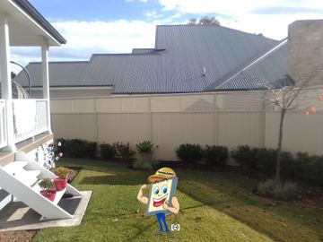 Cream Colorbond privacy fence behind a two-storey house with clipped hedges