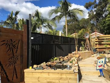 Charcoal Colorbond privacy fence beside a timber deck, rock garden and rusted decorative screen