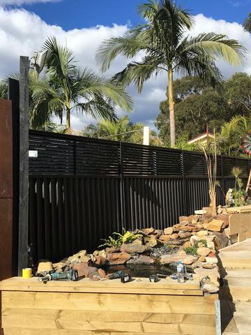 Charcoal Colorbond privacy fence beside a timber deck, rock garden and rusted decorative screen