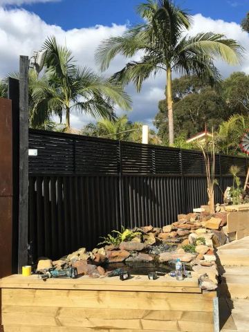 Charcoal Colorbond privacy fence beside a timber deck, rock garden and rusted decorative screen