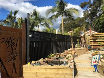 Charcoal Colorbond privacy fence beside a timber deck, rock garden and rusted decorative screen