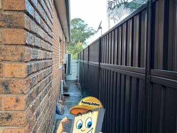 Dark Colorbond privacy fence filling a narrow side passage against a brick wall