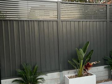 Charcoal Colorbond fence with a slat topper and planter boxes in the foreground