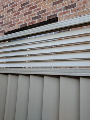 Close view of a cream Colorbond fence with a slat topper against a brick wall