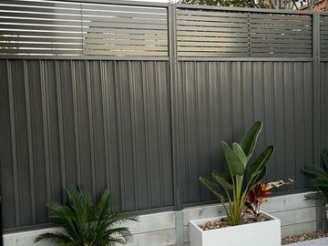 Charcoal Colorbond privacy fence with a slat extension and pot plants at the base