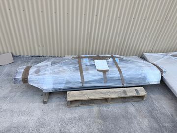 Plastic-wrapped charcoal slat frames sit on a timber pallet against cream corrugated sheeting on a concrete floor.