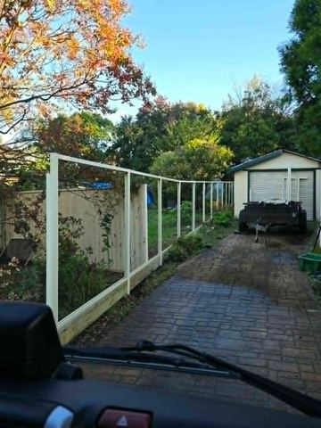 White tubular fence running beside a paved path toward a backyard shed