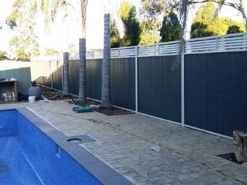 Dark Colorbond privacy fence with a white slat topper beside a swimming pool