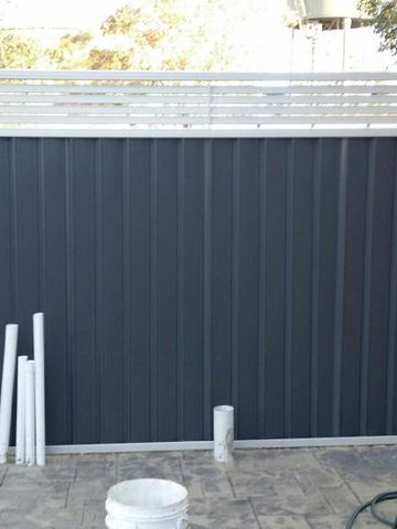 Dark Colorbond privacy fence with a white horizontal slat extension on a paved courtyard