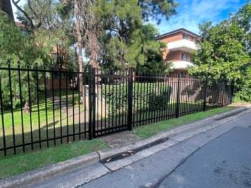 Black tubular front fence along a grassed corner beside the street