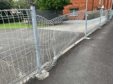 Crushed galvanised mesh panel sagging beside an asphalt driveway