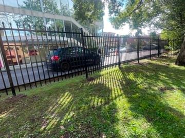 Black pickets with pointed finials step down a grassy bank toward a parked car and glass-fronted building.