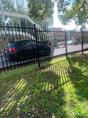 Black pickets with pointed finials step down a grassy bank toward a parked car and glass-fronted building.