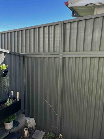 Monument panels with a shorter top infill section border a garden bed with planters beside a house eave.