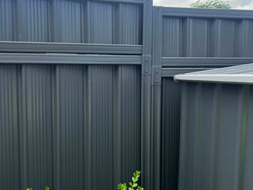 Stepped monument panels with a top infill section sit next to a charcoal corrugated garden shed over green shrubs.