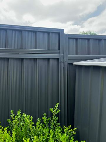 Stepped monument panels with a top infill section sit next to a charcoal corrugated garden shed over green shrubs.