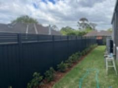Long monument boundary panels topped with horizontal louvre slats border a mulched garden bed on a green lawn.