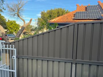 Charcoal Colorbond privacy fence stepping up a slope beside a white gate post