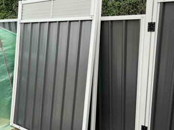 Charcoal ribbed sheets in a light grey frame include a gate with a louvre upper section in a leafy backyard.