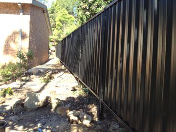 Long charcoal Colorbond privacy fence running along a dirt path