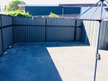 Dark corrugated panels turn a corner around a concrete utility yard with a matching gate and a rotary clothesline.