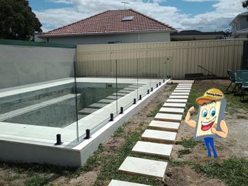 Tall cream corrugated steel runs behind spigot-mounted glass pool panels around an empty concrete pool on white tiles.
