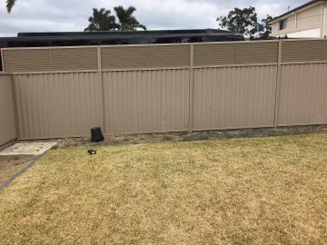 The scene shows a mid grey corrugated steel fence where an upper infill raises the height, sleepers form the base.