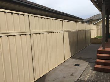 The scene shows a mid grey corrugated steel fence where an upper infill raises the height, sleepers form the base.