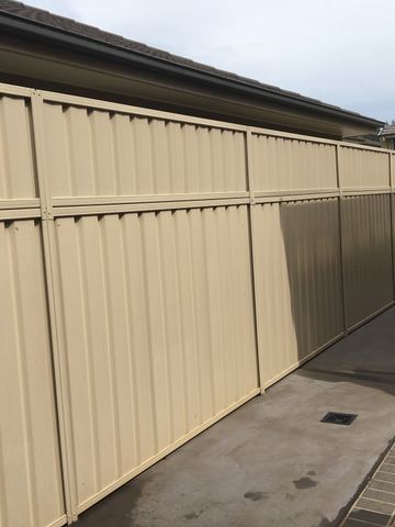 The scene shows a mid grey corrugated steel fence where an upper infill raises the height, sleepers form the base.