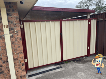 The scene shows a cream corrugated steel fence where concrete paving runs alongside.