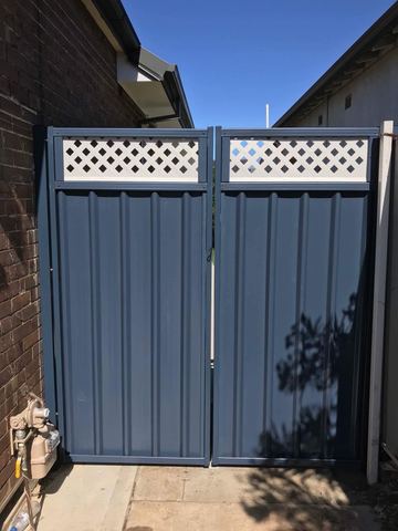 The scene shows a mid grey corrugated steel fence where residential buildings appear beyond the line.