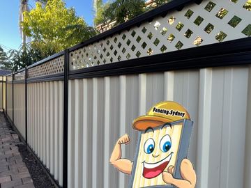 The scene shows a mid grey corrugated steel fence where lattice tops the panels, concrete paving runs alongside.